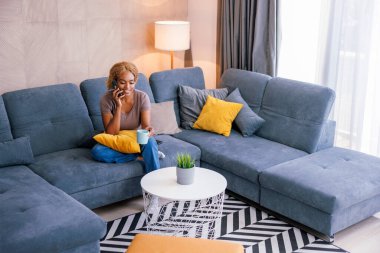 Güzel, genç bir kadın evde boş vakitlerin tadını çıkarıyor. Oturma odasındaki kanepede oturuyor, kahve içiyor ve akıllı telefon kullanarak telefon görüşmesi yapıyor.