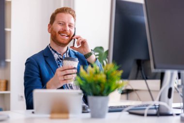 Sıradan bir iş adamı ofiste çalışırken telefonla konuşuyor ve kahve içiyor.