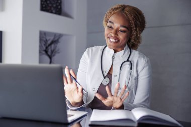 Kadın doktor, ev ofisinden, evden işe giderken hastayla çevrimiçi video görüşmesi yapıyor.