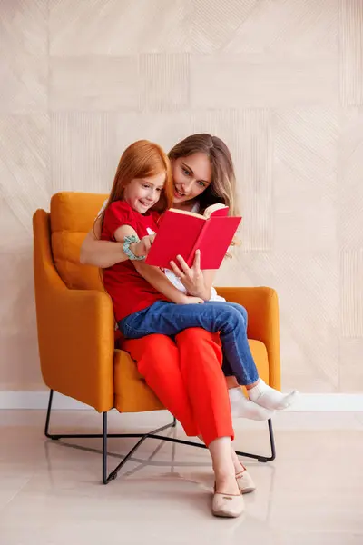 美丽的母亲和女儿坐在扶手椅上 母亲抱着女儿 抱着女儿 给她看书 — 图库照片