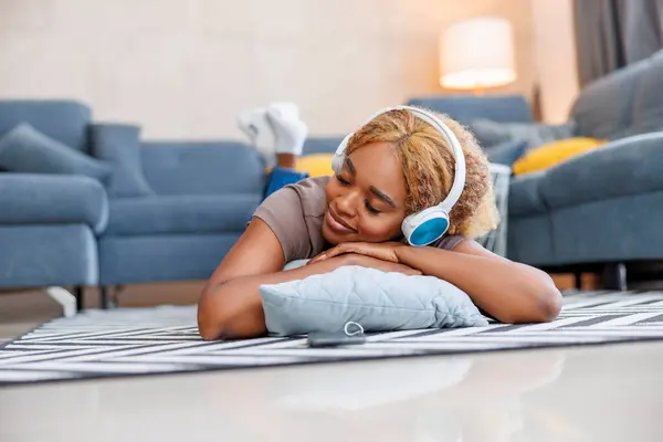 美丽的女人躺在地板上 头戴耳机 微笑着 一边听音乐 一边在家里放松 — 图库照片