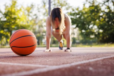 Spor kıyafetli genç bir kadının sabah antrenmanı olarak açık hava basketbol sahasında şınav çekmesi.