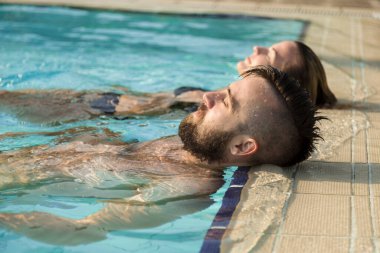 Birbirlerine aşık genç bir çift yüzme havuzunun kenarında yüzüyor, güneşleniyorlar.