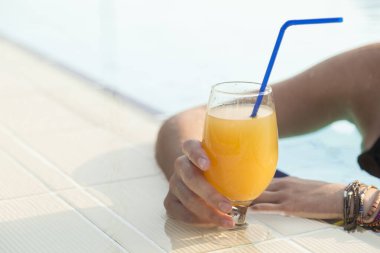 Güzel sarışın yüzme havuzunda eğleniyor, portakal suyu içiyor.