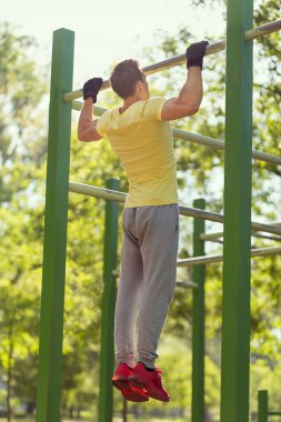 Kaslı, yapılı, genç bir sporcu açık hava spor salonunda çene çalıyor.