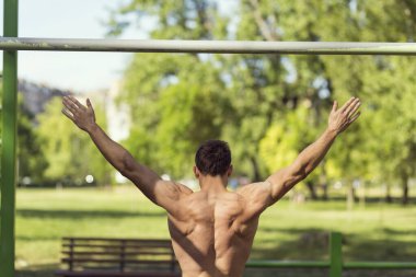 Kaslı, yapılı, genç bir sporcu açık hava spor salonunda çene çalıyor.