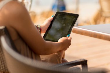 Güzel bir esmer açık hava kafede oturuyor, tablet bilgisayarında e-kitap okuyor ve limonata içiyor.