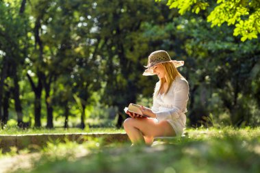 Parkta güneşli bir yaz gününde kitap okuyan genç bir kadın.