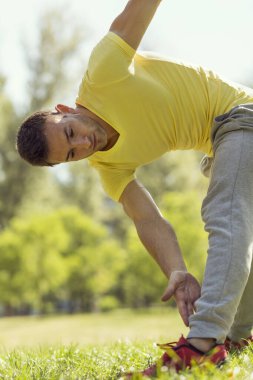 Genç sporcu parkta çalışıyor, koşmadan önce esniyor.