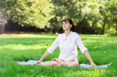 Orta yaşlı kadın Yoga sabah erken bir parkta yapıyor.