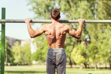 Kaslı, yapılı, genç bir sporcu açık hava spor salonunda çene çalıyor.