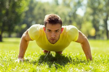 Parkta spor yapan genç bir sporcu, bir dizi şınav çekiyor.