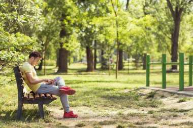 Sıkı bir antrenmandan sonra genç sporcu, parktaki ahşap bir bankta oturuyor, tablet bilgisayarda internette sörf yapıyor.