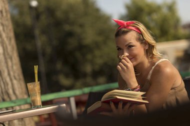 Nehir kıyısındaki bir kafede oturup kitap okuyan güzel genç bir kadın.