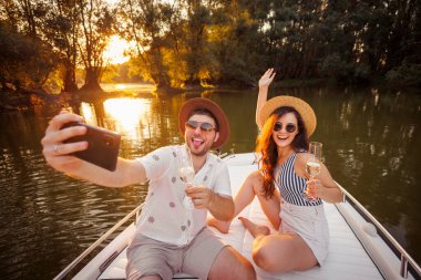 Güzel, aşık genç bir çift yaz tatilinde eğleniyor, selfie çekiyor ve kadeh kaldırıyor şampanya kadehlerini kaldırıyor bir tekneyle gün batımına yelken açıyorlar.