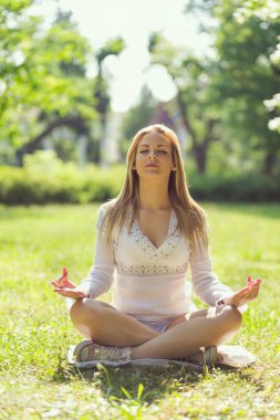 Güneşli bir yaz gününde parkta meditasyon yapan güzel genç bir kadın.