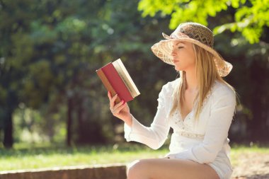 Parkta güneşli bir yaz gününde kitap okuyan genç bir kadın.