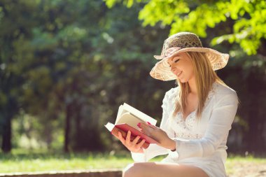 Parkta güneşli bir yaz gününde kitap okuyan genç bir kadın.