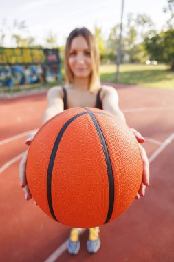 Spor giyim sektöründe aktif genç bir kadın basketbol sahasında basket oynayarak eğleniyor, topu tutuyor ve kameraya doğru gösteriyor.