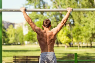 Kaslı, yapılı, genç bir sporcu açık hava spor salonunda çene çalıyor.