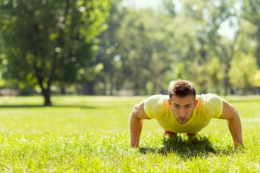 Parkta spor yapan genç bir sporcu, bir dizi şınav çekiyor.