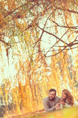 Birbirine aşık çiftler parktaki bir ağacın altında düşen sonbahar yapraklarında uzanıp doğada harika bir sonbahar gününün tadını çıkarıyorlar.
