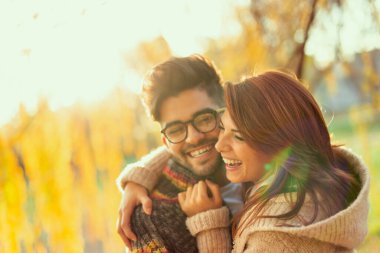 Genç aşık çift güneşli bir sonbahar gününde parkta gülüp eğleniyorlar.