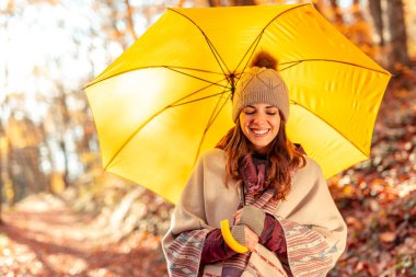 Güneşli bir sonbahar gününde orman yolunda yürürken dinlenen bir kadın renkli sonbahar yeşilliklerinin tadını çıkarıyor ve dışarıda vakit geçiriyor.