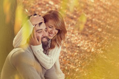 Birbirine aşık çiftler, sonbahar yaprakları üzerinde bir ağacın altındaki parkta oturup, harika bir sonbahar gününün tadını çıkarıyorlar.