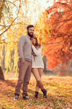 Birbirine aşık genç bir çift güneşli bir sonbahar gününde parkta sarılıp yürüyorlar.