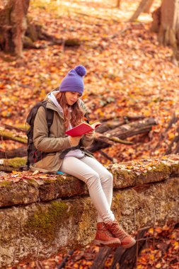 Aktif genç bir kadın kitap okurken yürüyüş yapıyor, dışarıda sonbahar günlerini geçirirken eğleniyor ve dinleniyor.