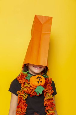 Cadılar Bayramı 'nda cadı gibi giyinmiş, kafasında turuncu bir alışveriş torbası olan, Cadılar Bayramı ve Kara Cuma' da eğlenen küçük kız.