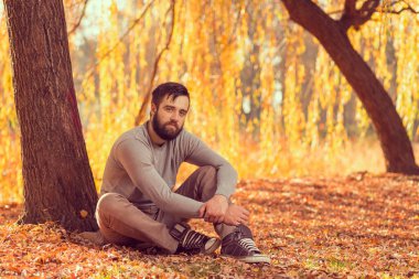 Parkta düşen sonbahar yapraklarında oturan yakışıklı genç adam, doğada huzur ve sessizliğin tadını çıkarıyor.