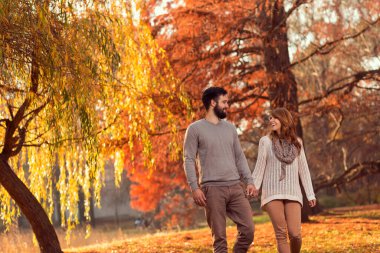 Birbirine aşık genç bir çift güneşli bir sonbahar gününde el ele tutuşup parkta yürüyor.