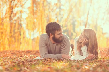Birbirine aşık bir çift, parktaki bir ağacın altında düşen sonbahar yapraklarında uzanıyor ve doğada harika bir sonbahar gününün tadını çıkarıyor. Bir adama odaklan.