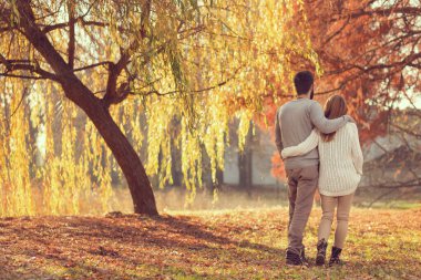 Birbirine aşık genç bir çift güneşli bir sonbahar gününde el ele tutuşup parkta yürüyor.