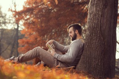 Genç yakışıklı bir adam, düşen sonbahar yapraklarında oturuyor, harita okuyor, seyahat macerasına hazırlanıyor.