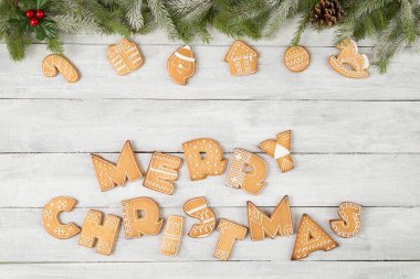Güzel dekore edilmiş Noel kurabiyelerinin üst manzarası harf şeklinde Mutlu Noeller çam dalları, şeker kamışı ve beyaz ahşap arka planda ökseotu