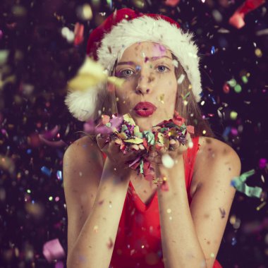 Noel Baba 'nın şapkasını takan güzel genç bir kadın, yılbaşı partisinde eğleniyor, konfetileri uçuruyor ve öpücükler yolluyor.