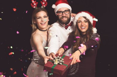 Bir grup genç arkadaş yeni yıl partisinde eğleniyor ve güzel paketlenmiş bir hediye kutusu tutuyorlar.