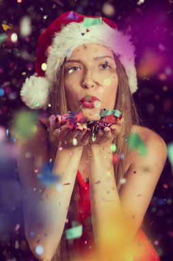 Noel Baba 'nın şapkasını takan güzel genç bir kadın, yılbaşı partisinde eğleniyor, konfetileri uçuruyor ve öpücükler yolluyor.