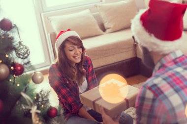 Birbirine aşık bir çift güzel dekore edilmiş bir Noel ağacının yanında oturma odasında oturuyor, Noel hediyelerini değiş tokuş ediyor ve eğleniyorlar.