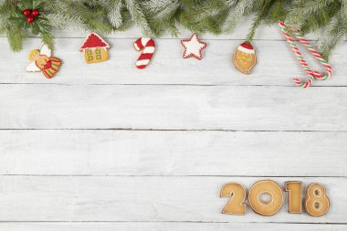 Güzel dekore edilmiş, köknar dalları ve beyaz ahşap arka planda ökseotu olan renkli Noel kurabiyelerinin üst görüntüsü. Numaralar 2018 ve kopyalama alanı