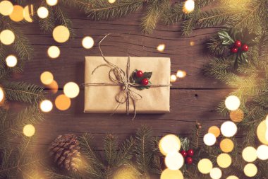 Çam dallarından yapılmış bir çerçeve ve Noel ışıklarından yapılmış güzel paketlenmiş bir hediye kutusu ahşap masaya yerleştirilmiş.