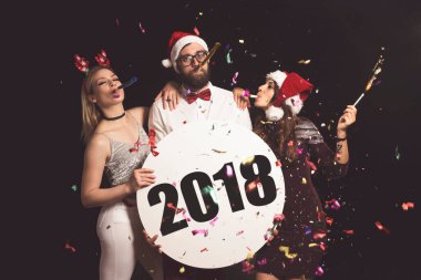 Bir grup arkadaş eğleniyor, Yeni Yıl arifesini kutluyorlar ve üzerinde 2018 yazılı karton bir daire tutuyorlar.