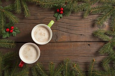 Ökseotu desenli bir çam dalında iki kahve fincanının masa üstü resmi.