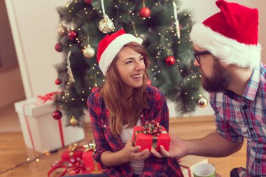 Güzel bir Noel ağacının yanında, oturma odasında oturmuş Noel hediyelerini değiş tokuş eden genç bir çift..