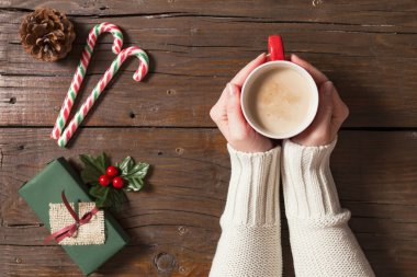 Birkaç Noel hediyesi ve dekorasyonun yanında bir fincan sıcak kahve tutan kadın elleri.