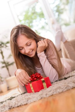 Güzel esmer halının üzerine uzanmış, hediyeyi açıyor.