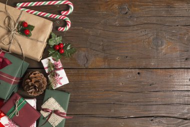 Güzel paketlenmiş Noel hediye kutuları, baston şekerler, çam kozalakları ve tahta bir masada ökseotu manzarası.